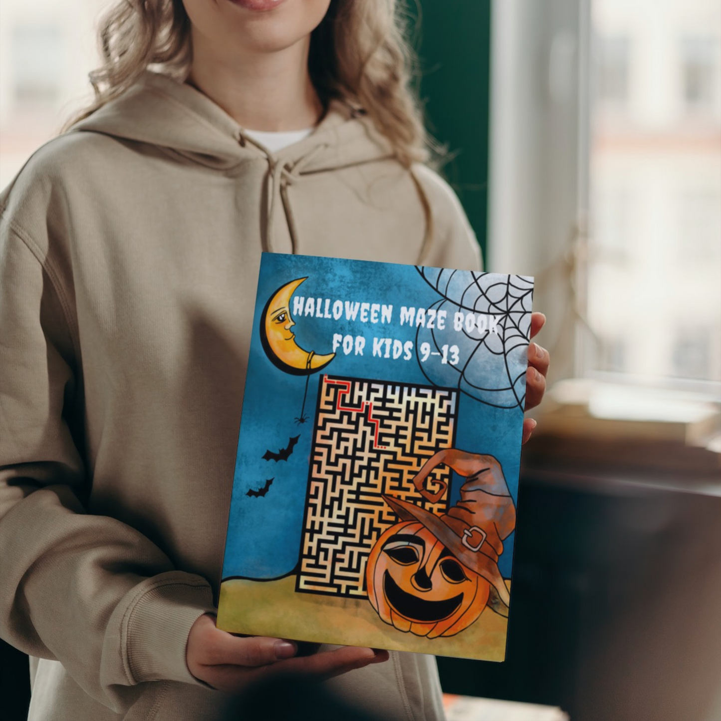 "Halloween Maze Book for Kids 9-13" by ArisaTeam in the hands of a girl.