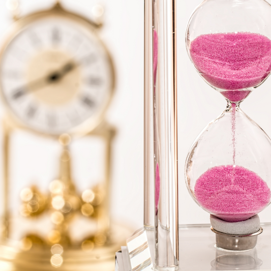 An hour glass with pink sand and a golden pillar clock symbolizing time management for the holiday season