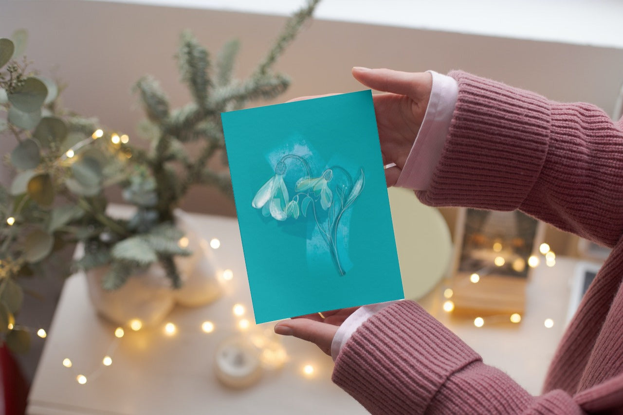 January Snowdrop birth flower greeting card held in hand with cozy holiday lights