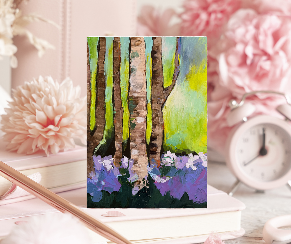 Woodland Serenity greeting card with impressionist forest artwork displayed on a desk with flowers and a clock in a soft lifestyle setting