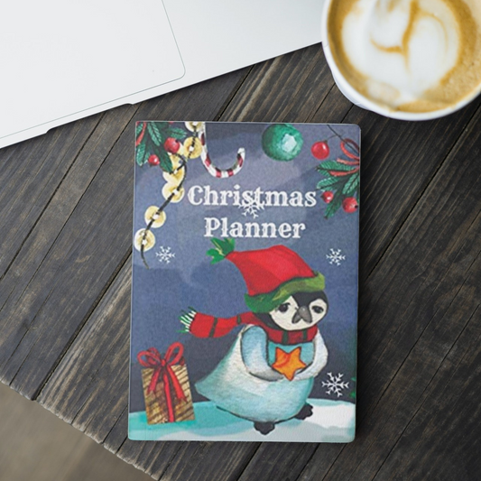 the penguin Christmas planner by arisateam with a penguin and Christmas ornaments in the cover design and close to a cup of coffee and a laptop