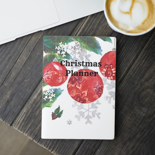 the ornaments Christmas planner by arisateam with ornaments, snowflakes, and leaves in the cover design and close to a cup of coffee and a laptop