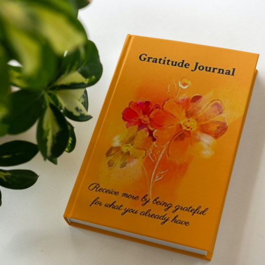 The hardcover version of the gratitude journal by Arisateam near a green plant.