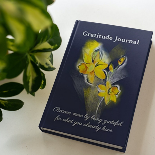 The hardcover version of the gratitude journal by Arisateam near a green plant.