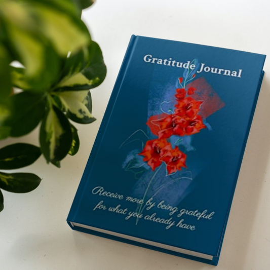 The hardcover version of the gratitude journal by Arisateam near a green plant.