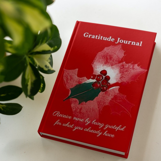 The hardcover version of the gratitude journal by Arisateam near a green plant.