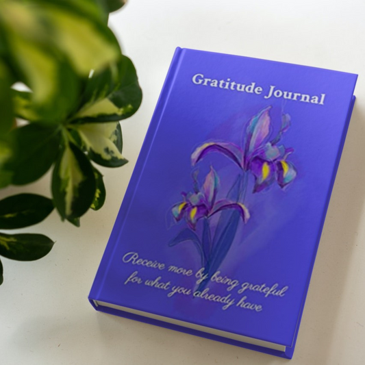 The hardcover version of the gratitude journal by Arisateam near a green plant.