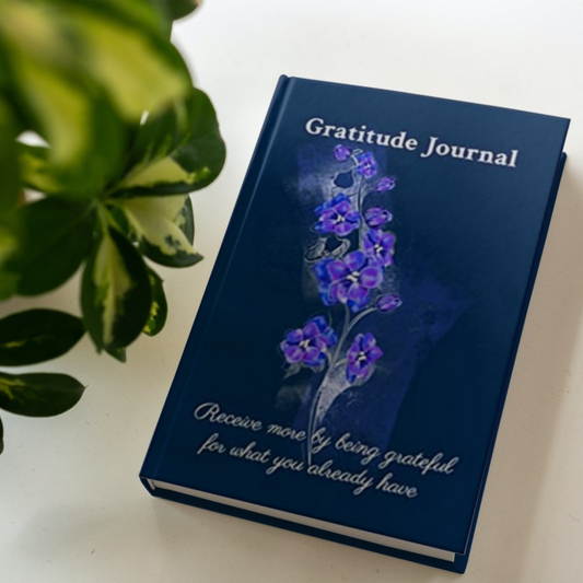 The hardcover version of the gratitude journal by Arisateam near a green plant.