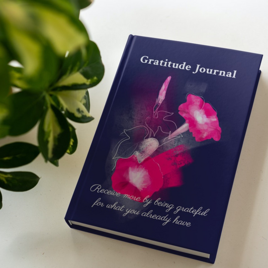 The hardcover version of the gratitude journal by Arisateam near a green plant.